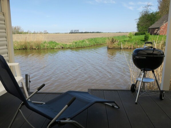 Una terraza con una silla y una parrilla, con vistas a un cuerpo de agua y campos.