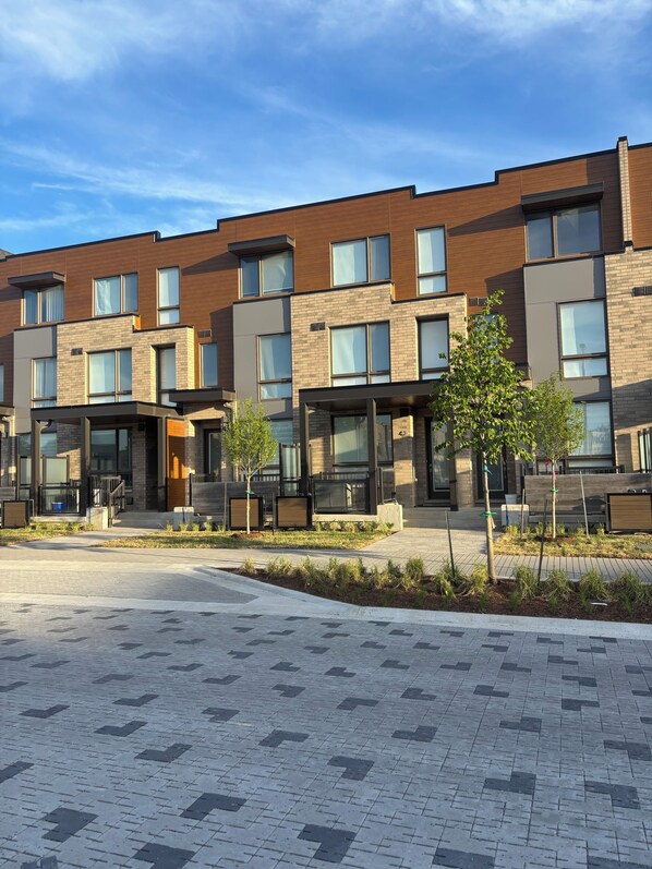 A modern multi-story building with a brick facade, large windows, and a paved courtyard.