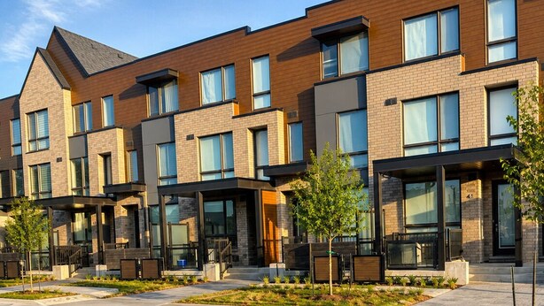 A modern multi-story residential building with a brick facade, large windows, and outdoor seating areas.