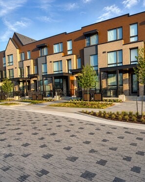 A modern multi-story residential building with a brick facade, large windows, and outdoor seating areas.