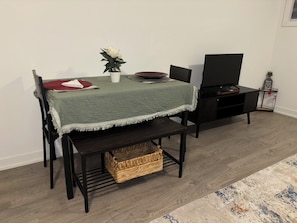 Un coin repas comprenant une table, des chaises, un meuble pour la télévision, un panier et une petite plante en pot.