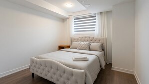 A bedroom with a bed, a nightstand, a window with blinds, and a ceiling light.