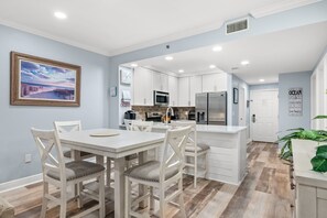 A modern kitchen with white cabinetry, a central island, and a dining area with white chairs.