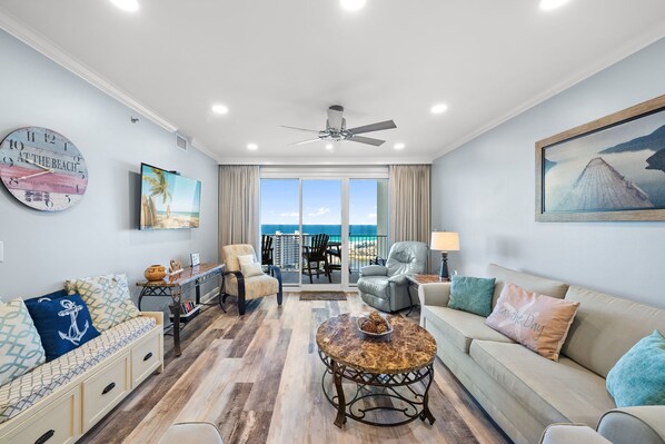 A spacious living room with a large window, a ceiling fan, and a view of the ocean.