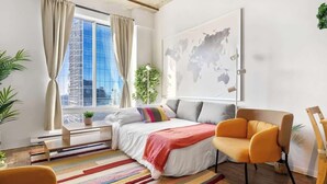 A modern bedroom with a large window, a bed with a colorful striped rug, a sofa, and a map on the wall. - Eminence Sleek Studio City View (Edmonton)
