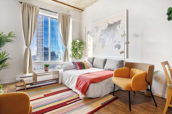 A modern bedroom with a large window, a bed with a colorful striped rug, a sofa, and a map on the wall.