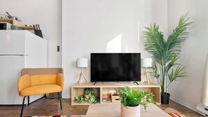 A modern living room with a sofa, a flat-screen TV, a coffee table, and a potted plant. - Eminence Sleek Studio City View (Edmonton)