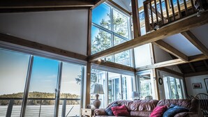 Ein geräumiger Raum mit großen Fenstern, einer Holzbalkendecke und einem Ledersofa mit Kissen.
