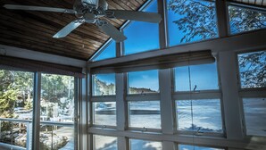 Ein Zimmer mit großen Fenstern, einem Deckenventilator und Blick auf eine verschneite Landschaft.