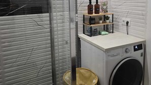 Ein kleiner Waschraum mit Waschmaschine, Wäscheständer und Regalen mit Flaschen und Behältern.