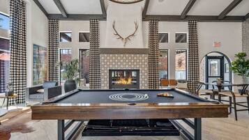 A pool table in a room with a fireplace, patterned walls, and large windows.