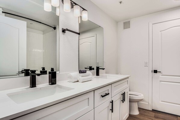 Un baño moderno con tocador blanco, grifos negros y un espejo grande.