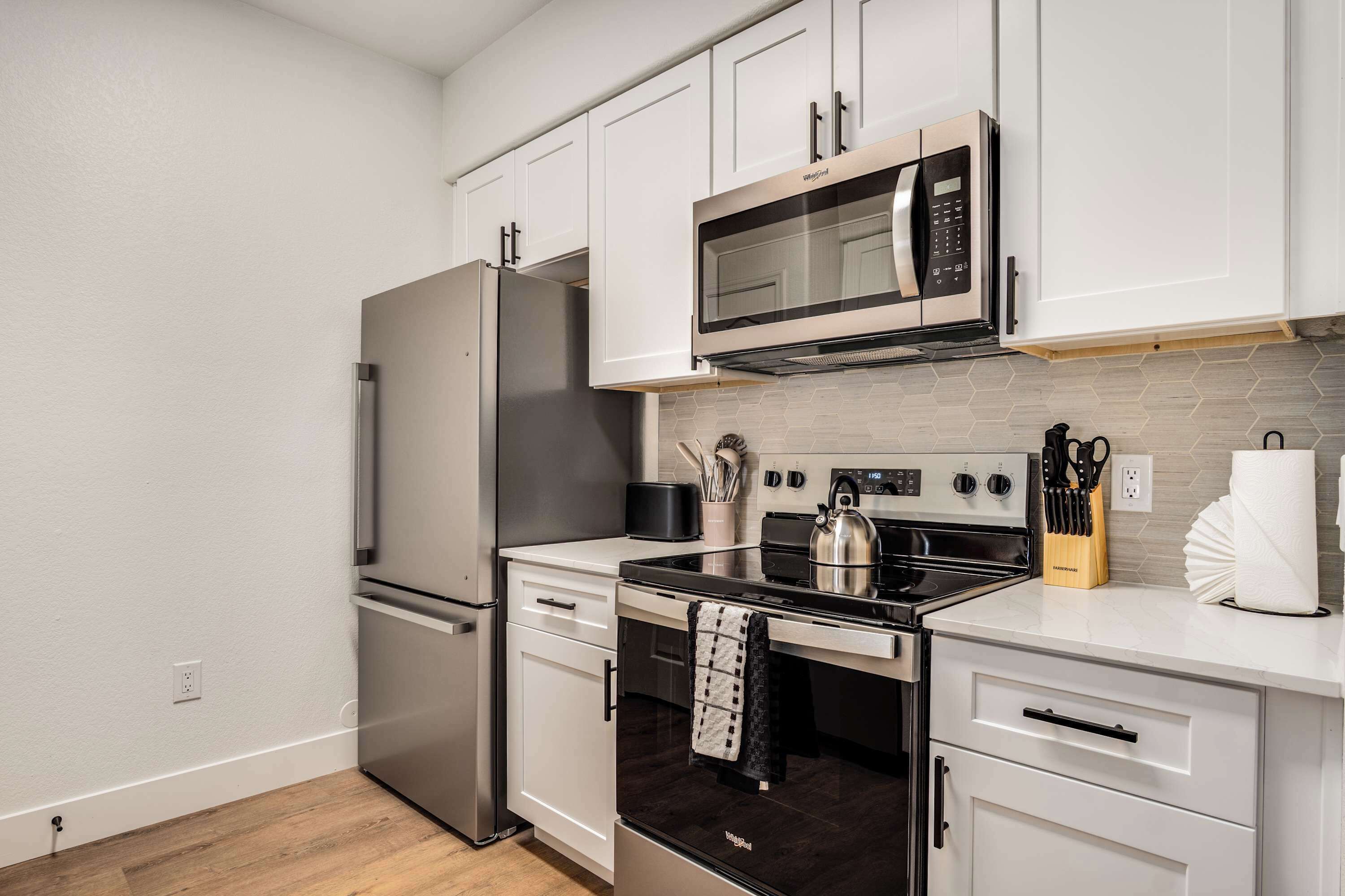 A modern kitchen with stainless steel appliances, white cabinetry, and a tiled backsplash.