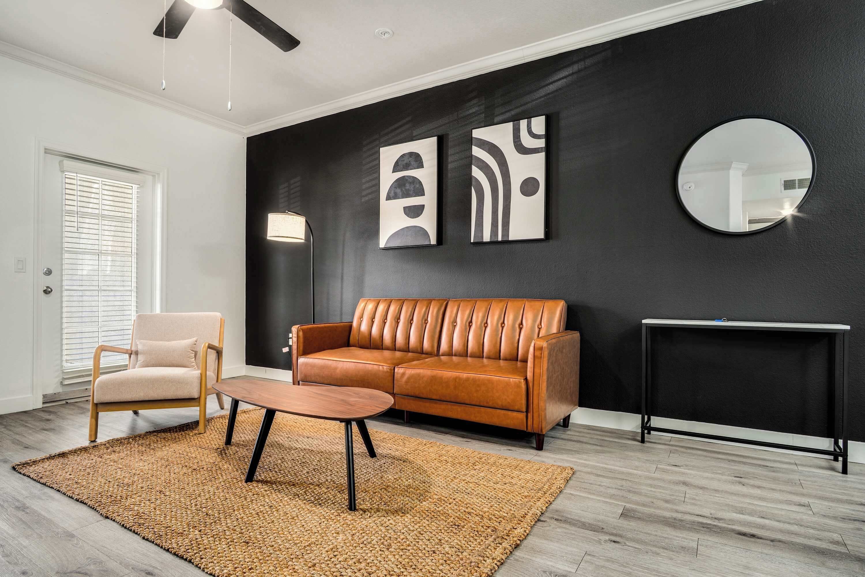 Een moderne woonkamer met een leren bank, een houten stoel, een ronde salontafel en een zwarte dressoir.
