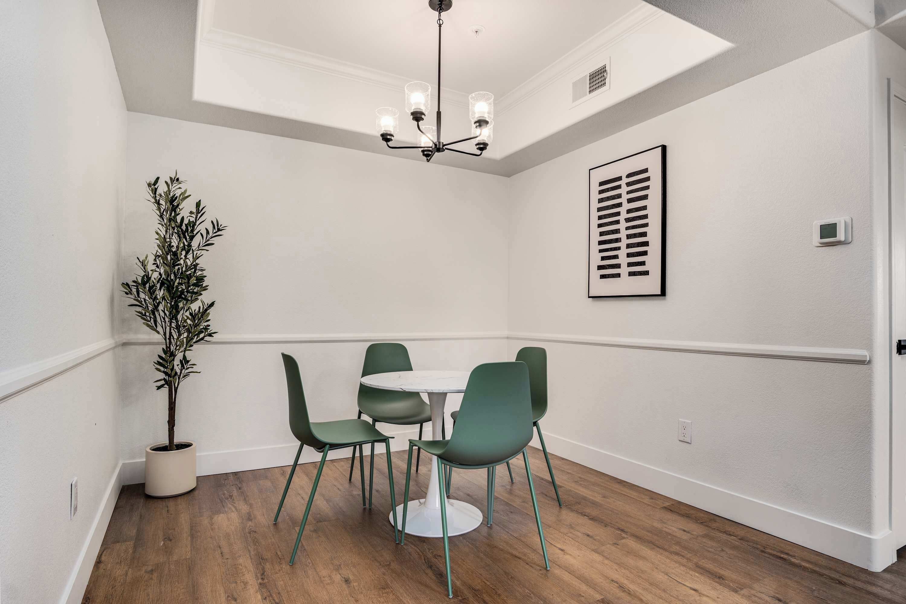 A dining area with a round table, four chairs, a potted plant, and a ceiling light fixture.
