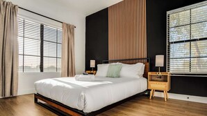 A modern bedroom with a large bed, wooden floor, and a nightstand with a lamp.