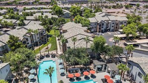 A residential area with a large swimming pool surrounded by lounge chairs and umbrellas, with multiple apartment buildings in the background.