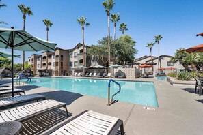 A pool area with lounge chairs, umbrellas, and palm trees. - Boulevard Stays Quiet Modern 1BR Pickleball, Pool, Parking, Gym 07 (Chandler)