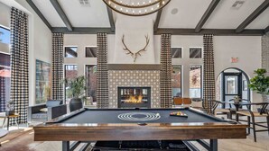 Una mesa de billar en una habitación con chimenea, paredes decoradas y ventanas amplias.