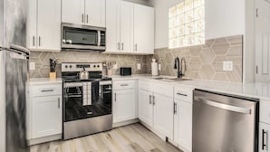 Una cocina moderna con armarios blancos, electrodomésticos de acero inoxidable, microondas, horno y lavavajillas.