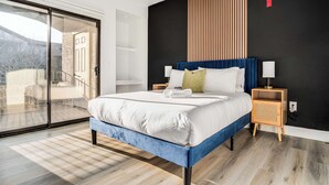 Un dormitorio moderno con una cama grande, un ventanal corredero a un balcón y una pared de acento oscura.
