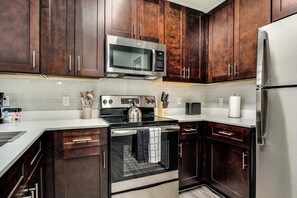 A kitchen with dark wooden cabinets, stainless steel appliances, and a white tiled backsplash. - Boulevard Stays 1BR by Stadium Pool, Parking, Gym 03 (Glendale)
