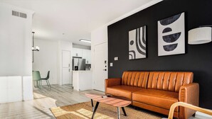 A modern living room with a leather sofa, a coffee table, and abstract wall art. - Boulevard Stays 1BR by Stadium Pool, Parking, Gym 03 (Glendale)