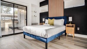A modern bedroom with a large bed, a sliding glass door, and a dark accent wall. - Boulevard Stays 1BR by Stadium Pool, Parking, Gym 03 (Glendale)