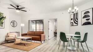 A modern living room with a sofa, coffee table, and chairs, a ceiling fan, and artwork on the walls.