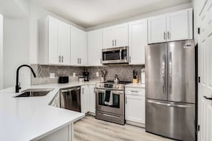 A modern kitchen with white cabinets, stainless steel appliances, and a herringbone tile backsplash.