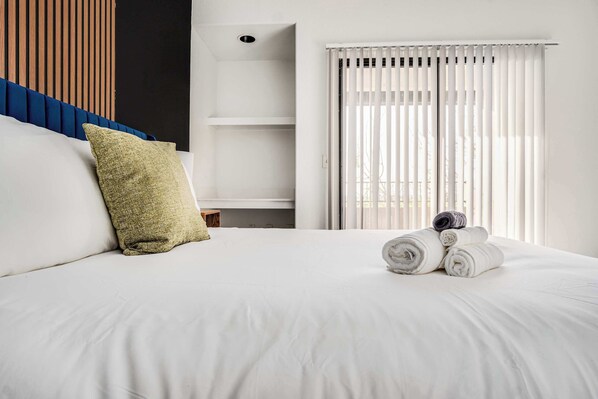 A neatly made bed with white linens, a green pillow, and rolled towels on the side.