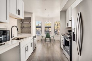 A modern kitchen with white cabinetry, a stainless steel refrigerator, and a view through large windows. - Boulevard Stays 2BR by Stadium Pool, Parking, Gym 08 (Glendale)