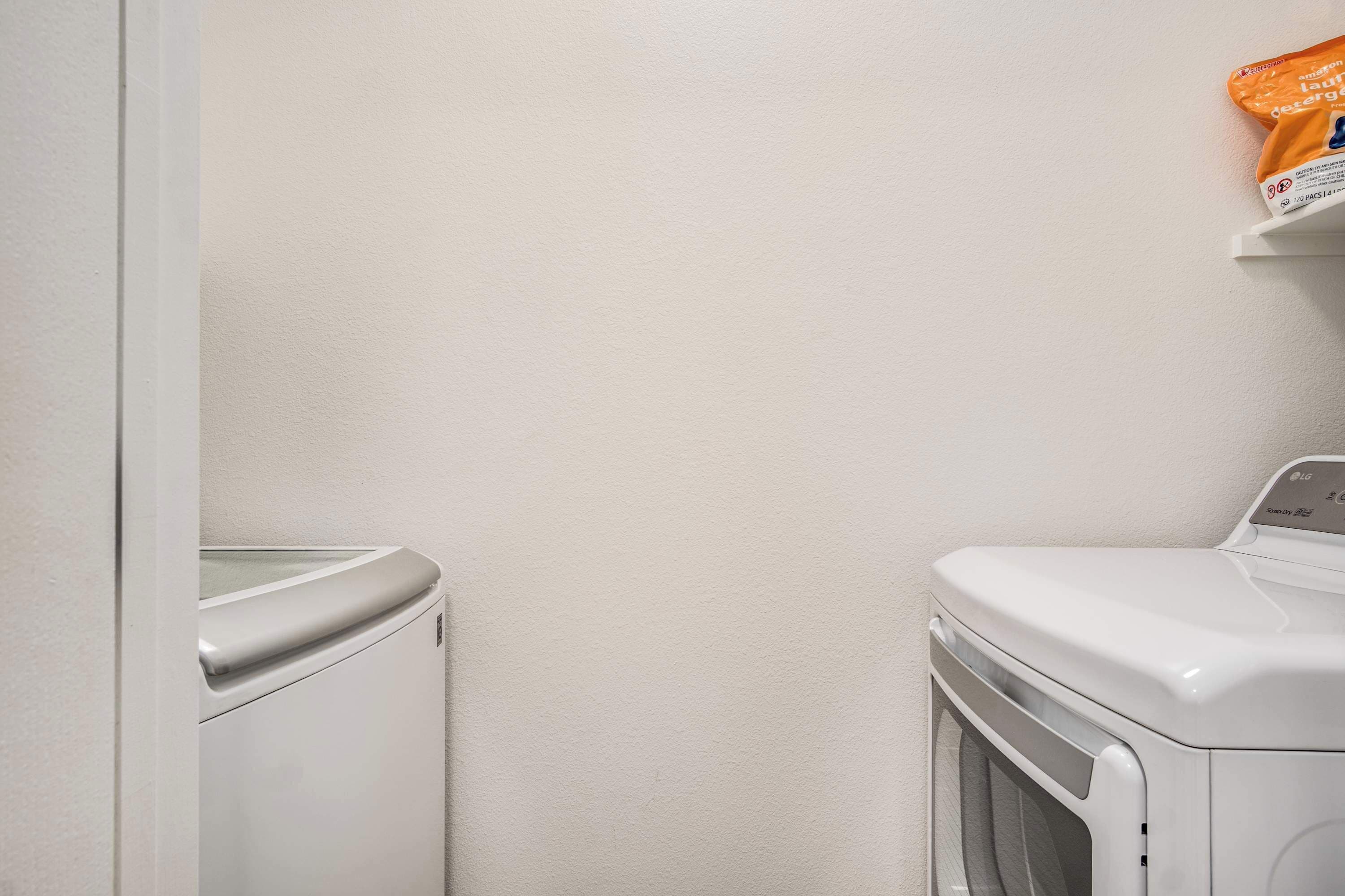 A laundry area with a washing machine and dryer, a white wall, and a shelf with a detergent package.