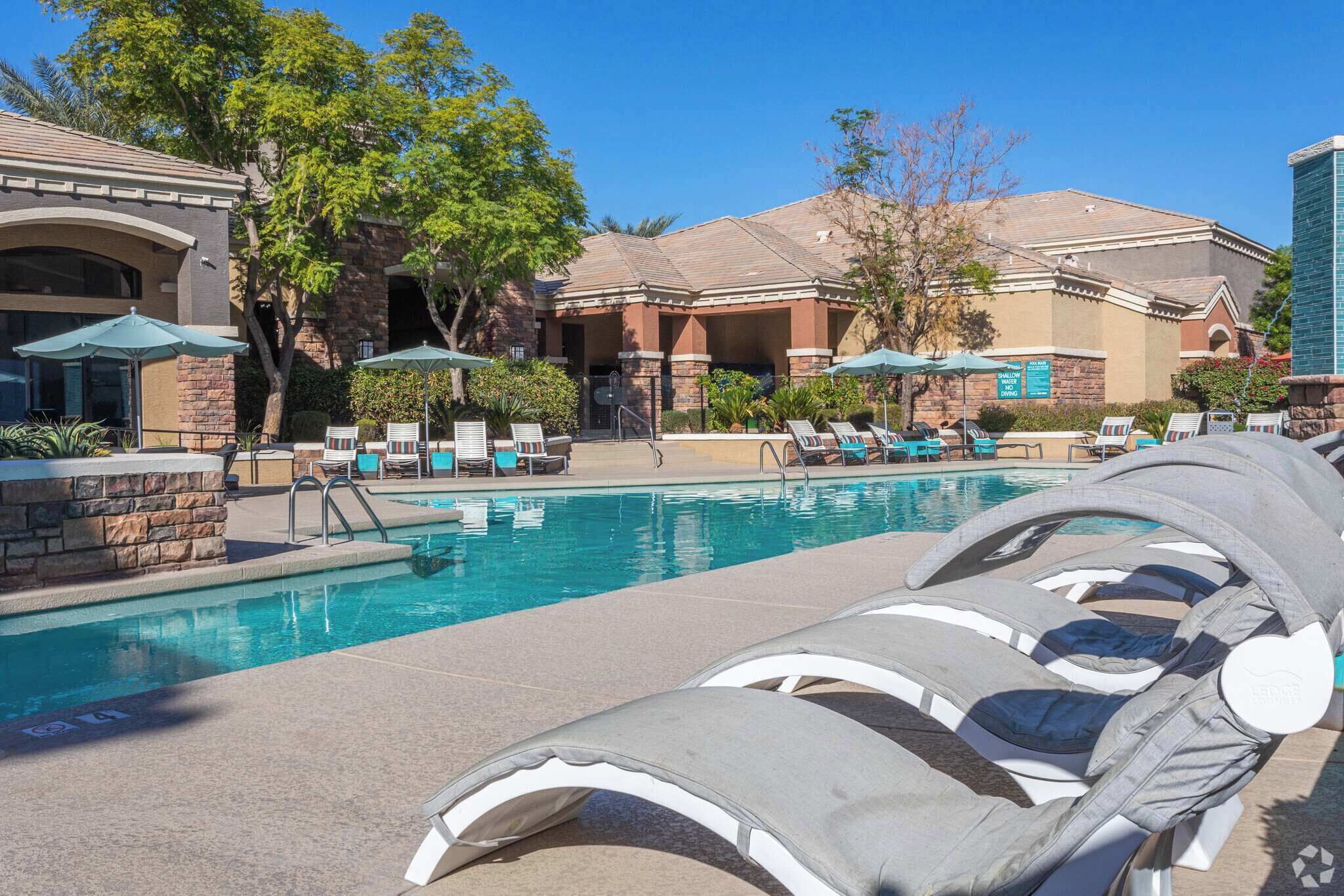 A pool area with lounge chairs, umbrellas, and a building with a stone facade.