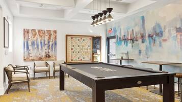 A pool table in a room with a chessboard, chairs, and abstract art on the walls.