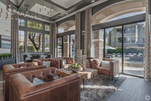 A spacious indoor area with leather sofas, a coffee table, and large windows offering views of a residential area.