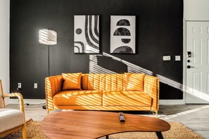 A modern living room with a sofa, a coffee table, and abstract wall art. - Boulevard Stays 1BR by the Stadium Pool, Parking, Gym 11 (Glendale)