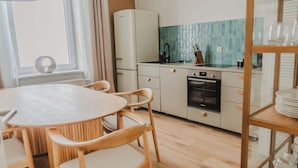 Une cuisine moderne avec un réfrigérateur blanc, un évier et une cuisinière. On y trouve une table à manger avec des chaises et une fenêtre avec des rideaux.