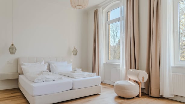 Une chambre moderne avec un grand lit, un petit coin salon et une fenêtre avec des rideaux.