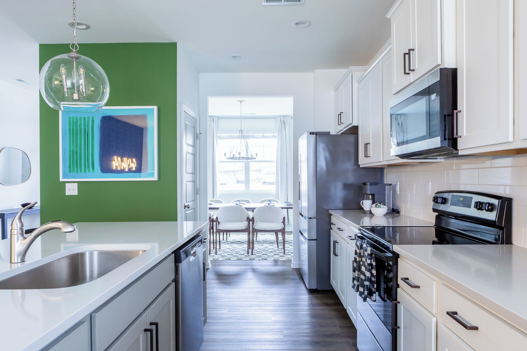 Une cuisine moderne avec des armoires blanches, des appareils en acier inoxydable et un mur d’accent vert.
