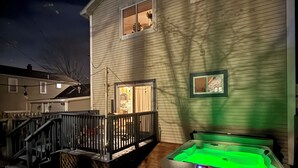 A house with a hot tub in the backyard, a wooden deck, and a staircase leading to the front door.