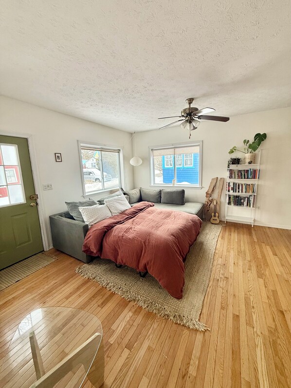 A bedroom with a bed, a ceiling fan, a bookshelf, and a view of the outside.