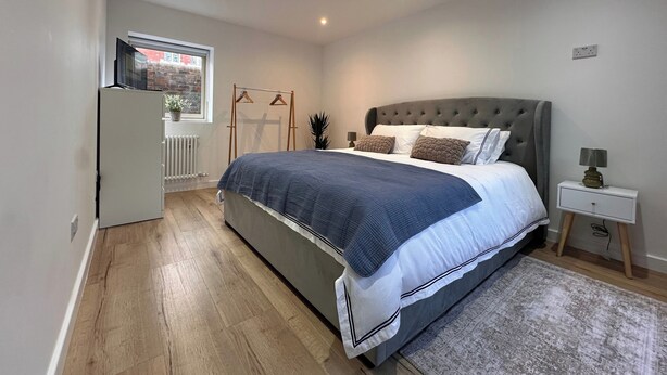 Une chambre à coucher avec un lit, une table de chevet, une lampe et une vue sur l’extérieur par une fenêtre.