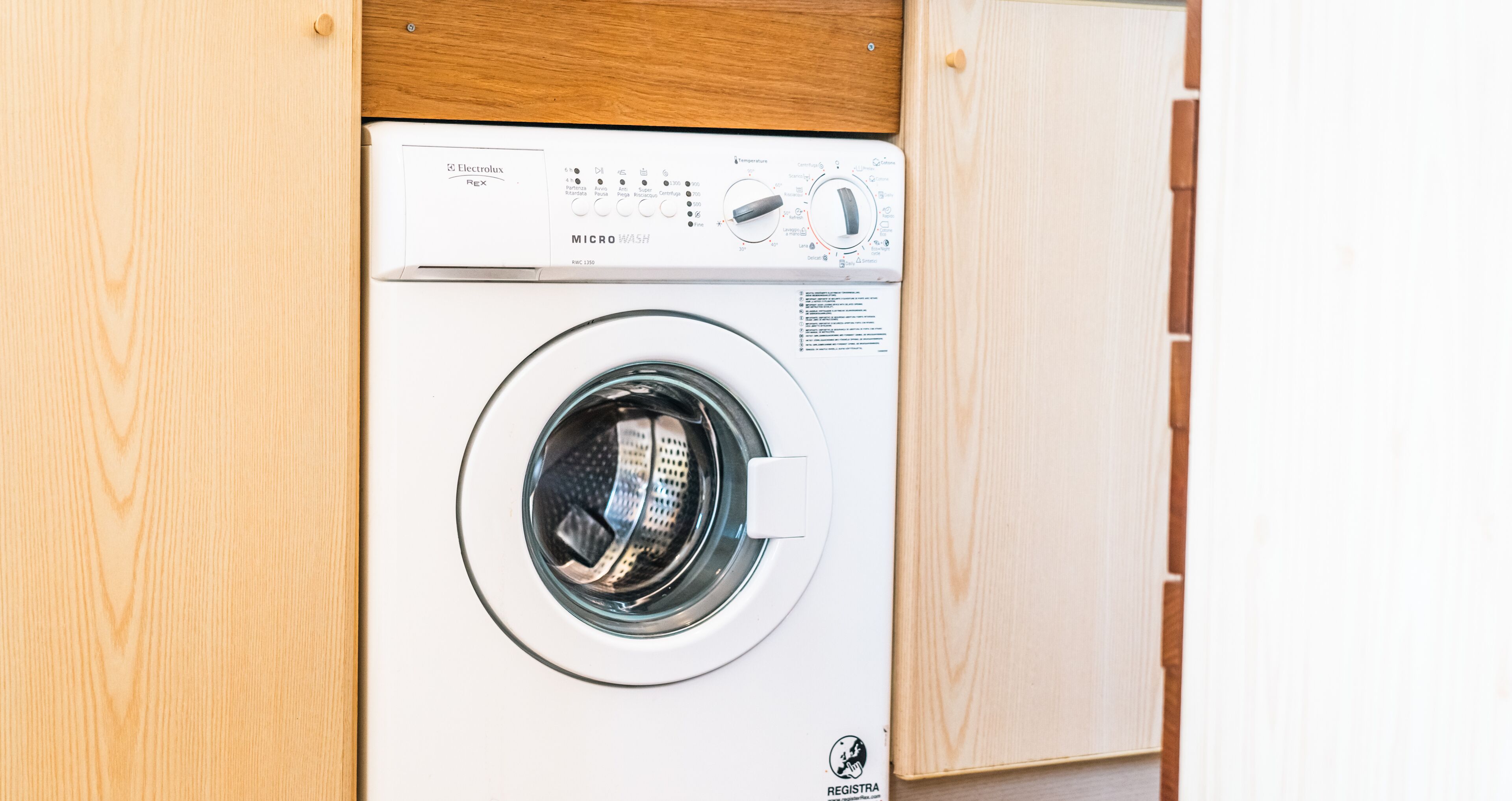 Vue de face d’un lave-linge, avec son panneau de commande et la porte en bois de son meuble.