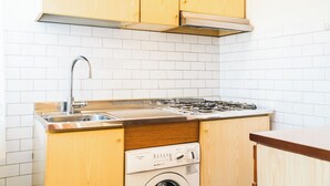 Ett kompakt kök med träskåp, en diskho i rostfritt stål och en inbyggd tvättmaskin.