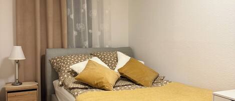 Un dormitorio ordenado con cama, mesita de noche, lámpara y un pequeño escritorio.