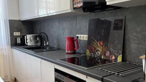 Cozinha moderna com armários brancos, bancada preta, chaleira vermelha e um quadro.