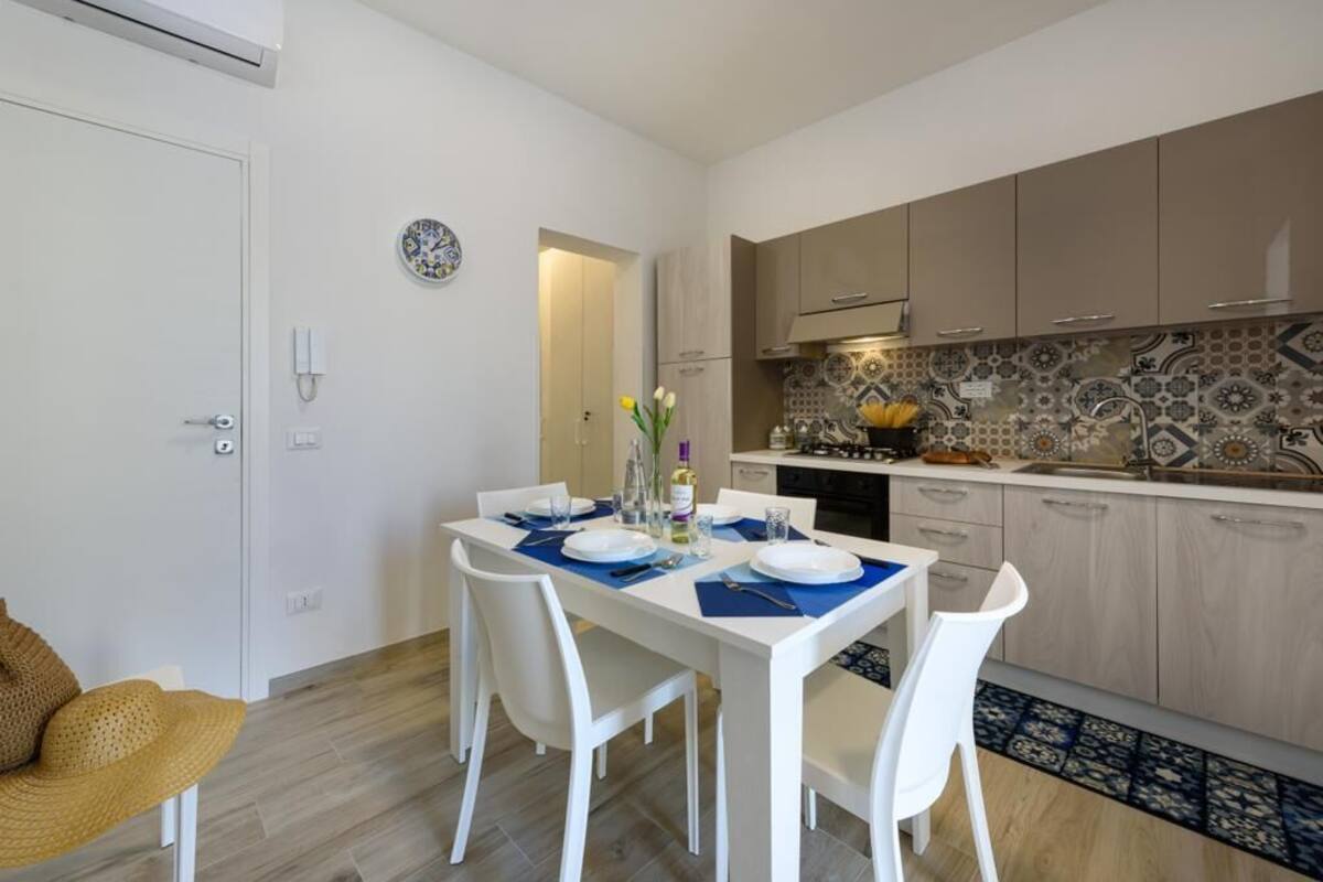 A modern kitchen with white cabinets, a tiled backsplash, and a dining area with a white table set for two.