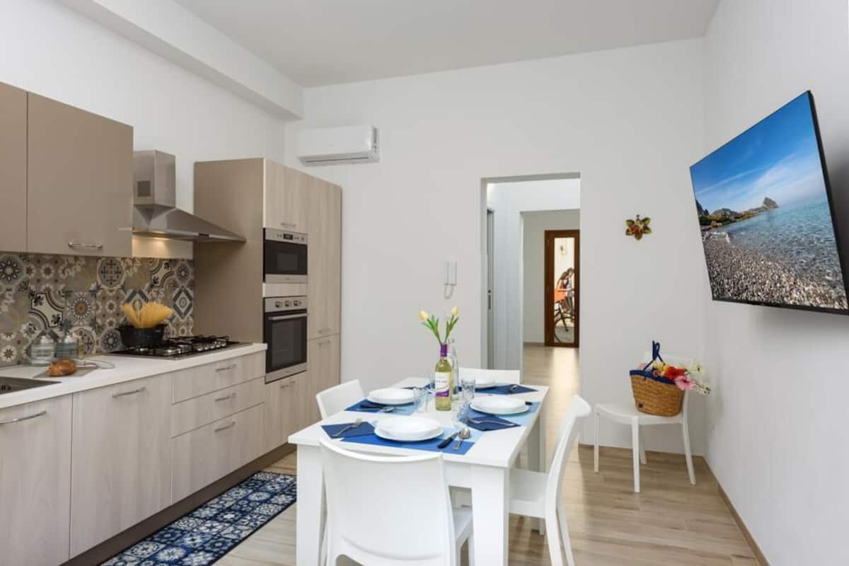 A modern kitchen with white cabinets, a dining area with a table set for two, and a large painting on the wall.