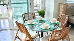 Un comedor con una mesa de vidrio, sillas de mimbre y vistas al exterior a través de un ventanal.